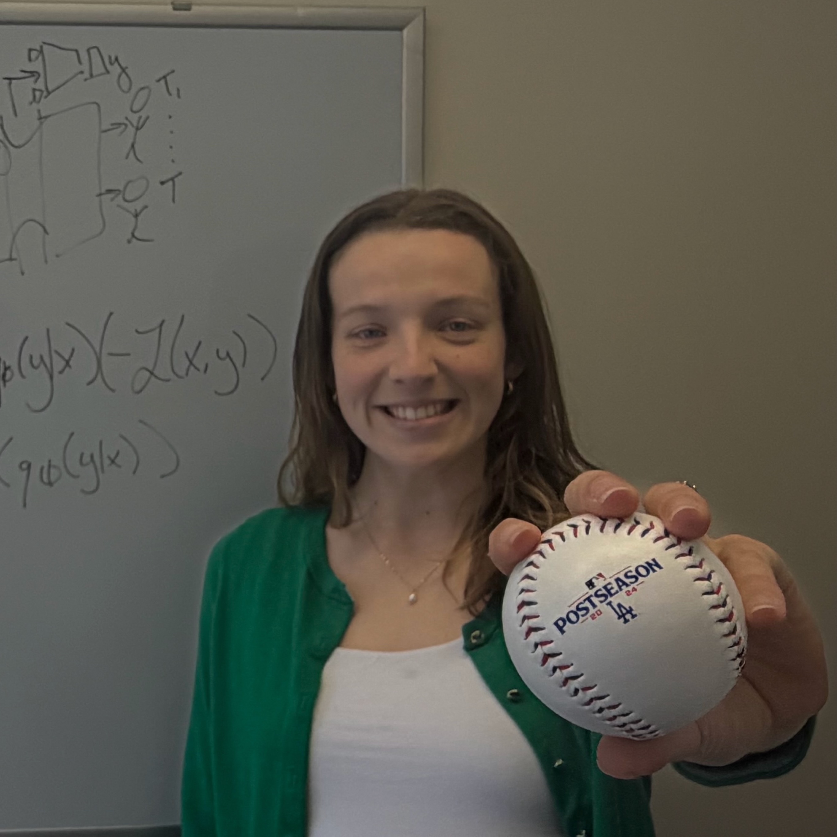 Mathilde Papillon standing in front of a whiteboard with mathematical diagrams, smiling and holding a Los Angeles Dodgers baseball toward the camera. Caption: Mathilde Papillon, a Ph.D. candidate in the Geometric Intelligence Lab at UC Santa Barbara, serves as an AI Research Scientist for the Los Angeles Dodgers.